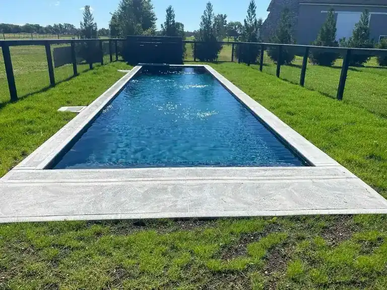 Long dark-finish pool with pale coping and a grass verge on both sides, a black fence and houses in the distance