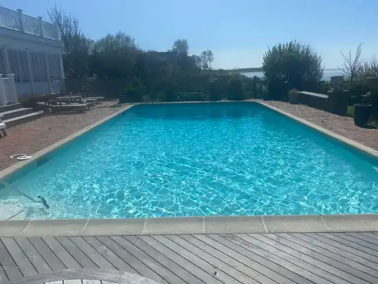 Large pool in clear turquoise water with a stone coping edge, an ipe deck in front and a brick terrace and water beyond