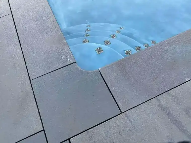 Corner of a pool with new stone coping and lit entry steps